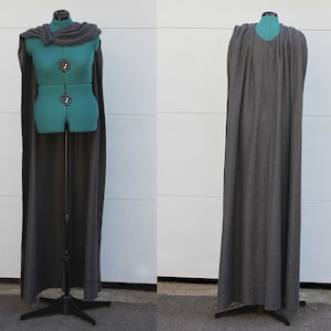 Puede incluir: Una capa gris oscuro exhibida en un maniqu&iacute; verde azulado. La capa es larga, llega hasta el suelo, y tiene un cuello de cisne drapeado. El maniqu&iacute; est&aacute; sobre un soporte de metal negro. La capa se muestra de frente y de espalda.