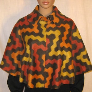 Op de afbeelding: Een bruine, oranje en gele gepatroneerde cape met een hoge kraag en een knoopsluiting. De cape is gemaakt van een zachte, pluche stof.