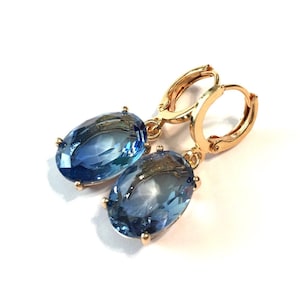 May include: A pair of gold hoop earrings with blue oval-shaped gemstones dangling from the hoops.