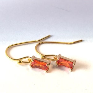 May include: A pair of gold earrings with orange rectangular gemstones. The earrings have a simple, minimalist design.
