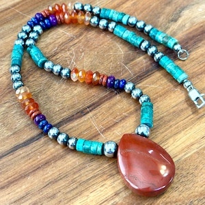 May include: A handcrafted necklace featuring a teardrop-shaped, reddish-brown pendant. The necklace incorporates turquoise, silver-colored beads, and a variety of colorful gemstone beads in shades of orange, purple, and blue. The necklace is secured with a silver clasp.