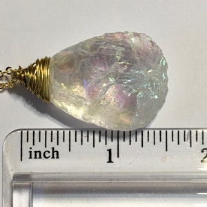 Pu&ograve; includere: Un ciondolo di cristallo bianco iridescente avvolto in filo d'oro, appeso a una catena d'oro. Il ciondolo &egrave; lungo circa 2,5 cm.