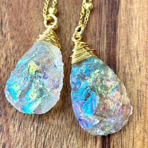 Pu&ograve; includere: Due ciondoli a goccia di cristallo iridescente su catene dorate. I cristalli sono avvolti in filo d'oro e hanno un bagliore arcobaleno.
