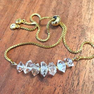 May include: A gold chain bracelet with a sliding clasp and a row of clear quartz crystals.