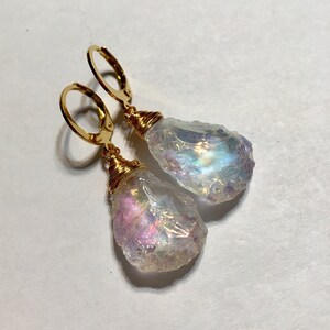 May include: A pair of gold earrings with iridescent teardrop-shaped crystals. The crystals are wrapped in gold wire and hang from gold hoops.