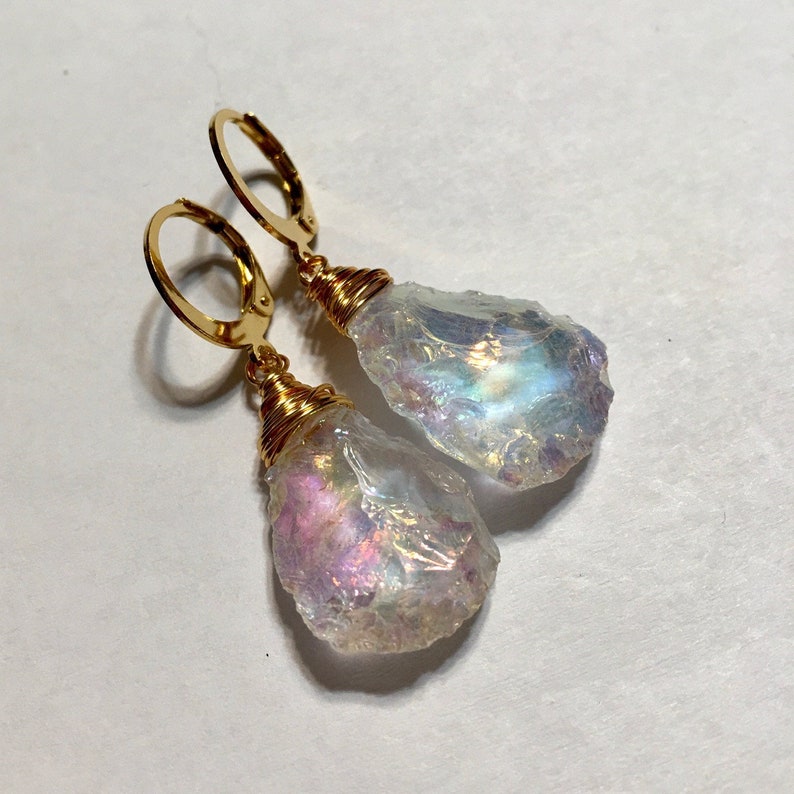 May include: A pair of gold earrings with iridescent teardrop-shaped crystals. The crystals are wrapped in gold wire and hang from gold hoops.