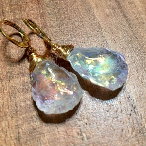 May include: A pair of gold earrings with iridescent white crystal teardrop dangles. The crystals are wrapped in gold wire and the earrings have gold lever back closures.
