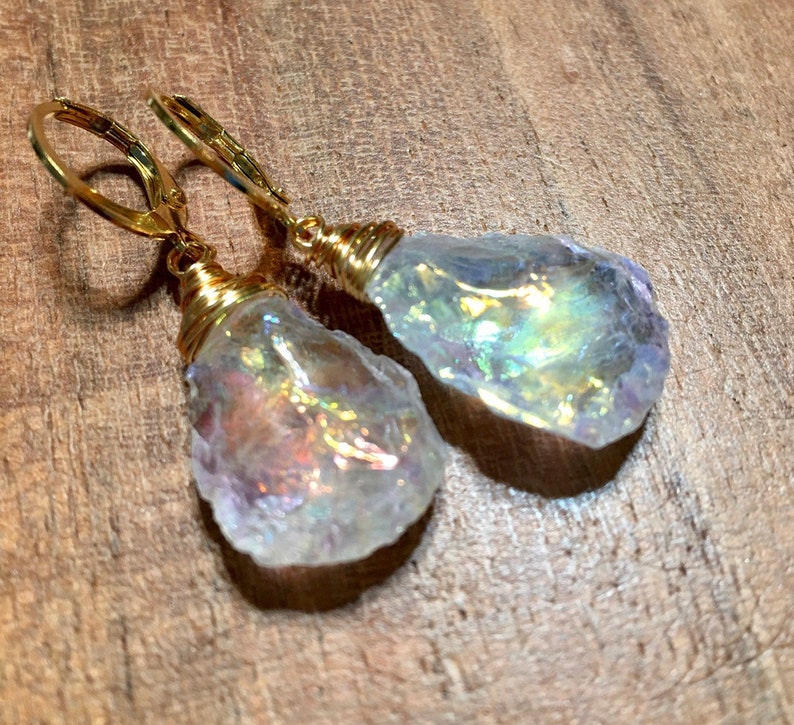 May include: A pair of gold earrings with iridescent white crystal teardrop dangles. The crystals are wrapped in gold wire and the earrings have gold lever back closures.