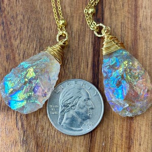 Pu&ograve; includere: Due ciondoli di cristallo iridescente su catene dorate. I cristalli sono avvolti in filo d'oro e hanno una forma a goccia. I ciondoli sono appesi su uno sfondo di legno.