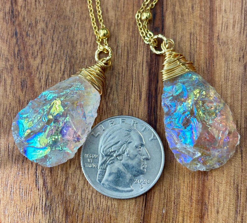Pu&ograve; includere: Due ciondoli di cristallo iridescente su catene dorate. I cristalli sono avvolti in filo d'oro e hanno una forma a goccia. I ciondoli sono appesi su uno sfondo di legno.