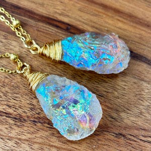 Pu&ograve; includere: Due ciondoli di cristallo iridescente avvolti in filo d'oro, appesi a catene d'oro. I cristalli sono trasparenti con un bagliore arcobaleno.