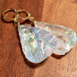 Pu&ograve; includere: Un paio di orecchini di cristallo iridescente con cerchi d'oro. I cristalli sono trasparenti con un bagliore arcobaleno.