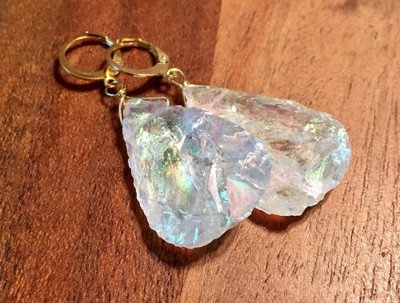 Pu&ograve; includere: Un paio di orecchini di cristallo iridescente con cerchi d'oro. I cristalli sono trasparenti con un bagliore arcobaleno.