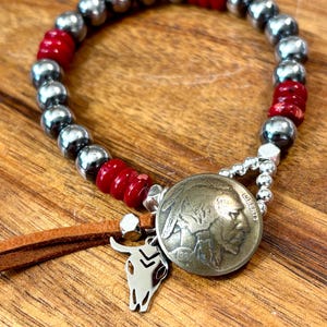 May include: A silver and red beaded bracelet with a silver buffalo nickel charm, a silver skull charm, and a brown leather tassel.