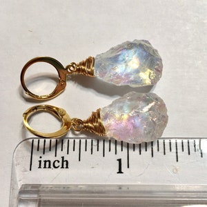 May include: A pair of gold earrings with iridescent white crystal drops. The earrings are approximately 1 inch long.