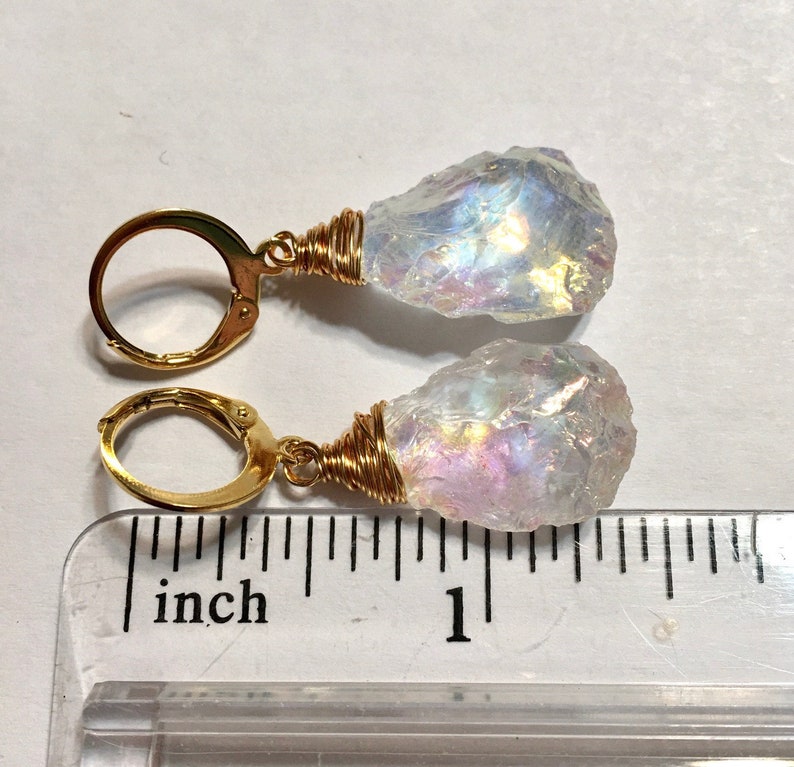 May include: A pair of gold earrings with iridescent white crystal drops. The earrings are approximately 1 inch long.