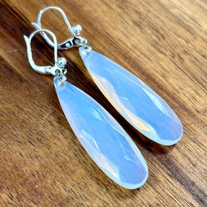 May include: A pair of silver teardrop earrings with iridescent white opal stones.