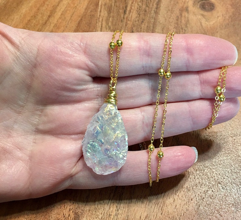 Pu&ograve; includere: Una collana con catena dorata con un grande ciondolo a forma di lacrima in cristallo bianco iridescente.