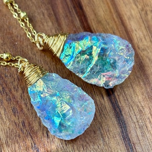 Pu&ograve; includere: Due ciondoli di cristallo iridescente su catene dorate. I cristalli sono avvolti in filo d'oro e hanno una forma a goccia.