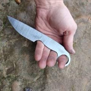 May include: A hand holding a small, silver knife with a rounded handle and a hole in the blade.