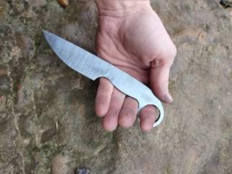 May include: A hand holding a small, silver knife with a rounded handle and a hole in the blade.