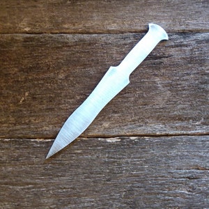 May include: A silver knife with a pointed tip and a rounded handle. The knife is lying on a wooden surface.