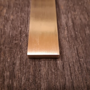 May include: A long, thin, rectangular piece of brass with a brushed finish. The brass is a warm, golden color.