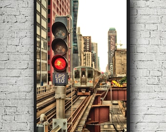 May include: A red traffic light with the words "LP2 110" on it is positioned at a railroad crossing. A train is passing by in the background. The scene is set in an urban environment with tall buildings.