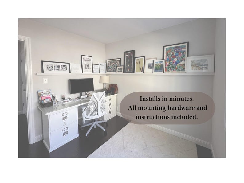 May include: A home office setup with a white desk, chair, and a computer monitor. A shelf above the desk displays framed artwork. The room has a neutral color palette with a rug and dark flooring. Text on the image: Installs in minutes. All mounting hardware and instructions included.