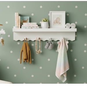 May include: A white scalloped shelf with baby items against a green polka dot wall. Items include books, a framed picture, a succulent, rolled towels, a mustard-colored sweater, a wooden teething ring, gray baby booties, and a hooded blanket.