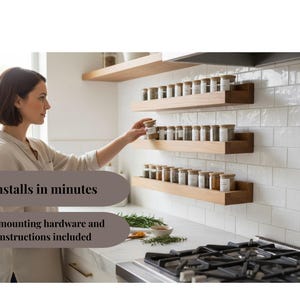 May include: A woman reaching for a spice jar on a wooden shelf. The kitchen features three wooden spice racks mounted on a white tiled wall. Each shelf holds multiple spice jars with wooden lids. The text "Installs in minutes" is visible.