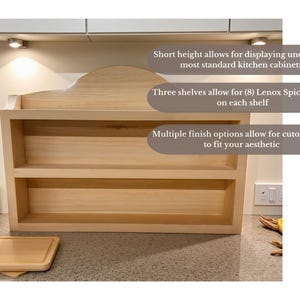May include: A light-colored wooden spice rack with three shelves. The text on the image says: "Short height allows for displaying underneath most standard kitchen cabinetry", "Three shelves allow for (8) Lenox Spice Houses on each shelf", and "Multiple finish options allow for cutomization to fit your aesthetic."