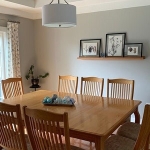 May include: A light gray dining room with a wooden table and chairs. The table is set with blue and white ornaments. There are four framed botanical prints on a shelf above the table.