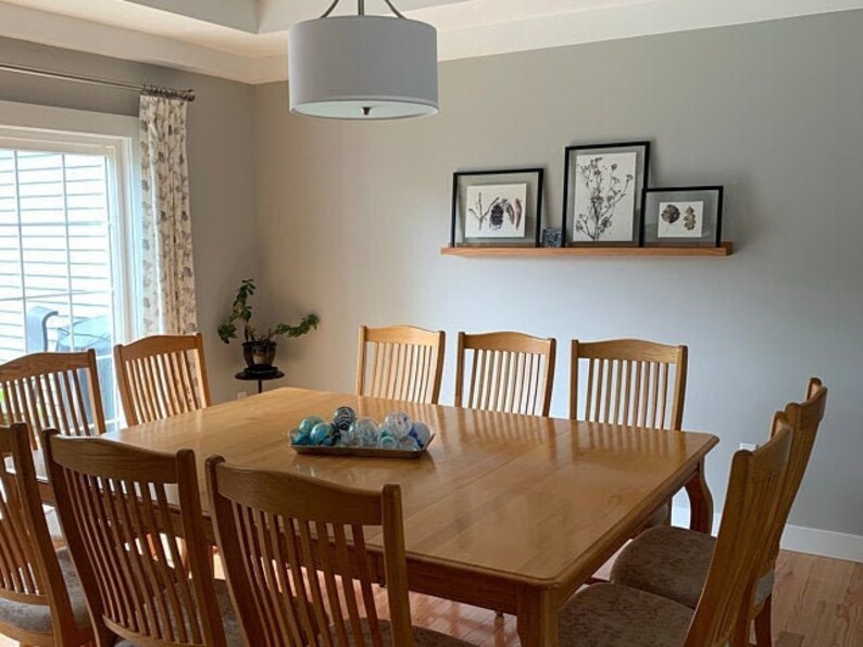 May include: A light gray dining room with a wooden table and chairs. The table is set with blue and white ornaments. There are four framed botanical prints on a shelf above the table.