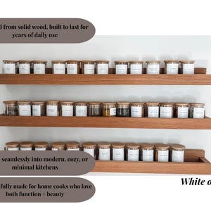 May include: Three wooden shelves with glass spice jars and wooden lids. The shelves are made of white oak and are mounted on a white wall. The jars have white labels. The text in the image says "Crafted from solid wood, built to last for years of daily use."