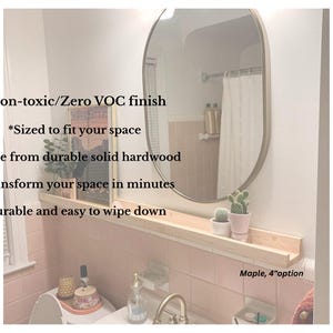 May include: A light-colored wooden shelf, 4 inches wide, installed above a pink-tiled bathroom wall. The shelf holds small potted plants and a framed picture. Text on the image says: Non-toxic finish, sized to fit your space, made from hardwood.