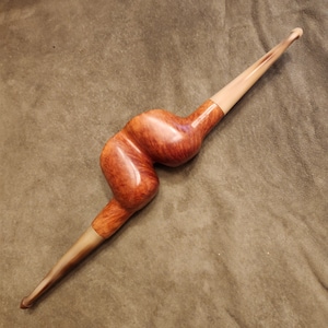 Könnte beinhalten: Eine braune und beigefarbene Holzpfeife mit einem einzigartigen, geschwungenen Design. Die Pfeife ist aus Naturmaterial gefertigt und hat eine glatte Oberfläche.