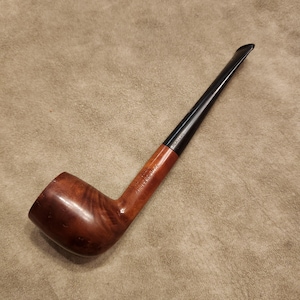 Puede incluir: Una pipa de tabaco de madera con un cuenco marrón oscuro y una boquilla negra. La pipa tiene un diseño curvo y un acabado liso y pulido. Las palabras "ANGELERS PIPE" están grabadas en el vástago.