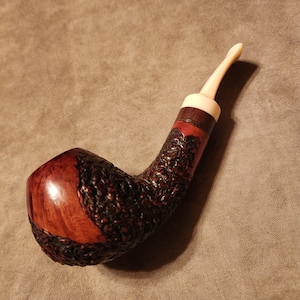 May include: A brown and black briar pipe with a white mouthpiece. The pipe has a rustic finish and a curved stem.