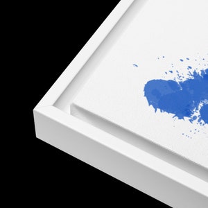 K&ouml;nnte beinhalten: Ein wei&szlig;er Leinwanddruck mit einem blauen Aquarell-Spritzer-Design. Die Leinwand ist mit einem wei&szlig;en Holzrahmen gerahmt.