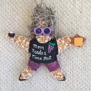May include: A starfish ornament with a purple and black shirt that says "Mom needs a time out" and a glass of wine in one hand and a cheese wedge in the other. The starfish has a purple and pink glitter finish and is wearing pink sunglasses.