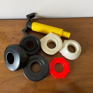 K&ouml;nnte beinhalten: Ein Set aus sechs bunten Spielzeug aus Plastik, darunter eine gelbe und schwarze Pumpe, ein wei&szlig;er Ring, ein roter Ring und drei schwarze Ringe. Das Spielzeug ist f&uuml;r Kinder zum Spielen gedacht.