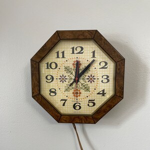 May include: A brown octagonal clock with a white face and black numbers. The clock has a floral design and the text "Sunbeam Electric Made in U.S.A."