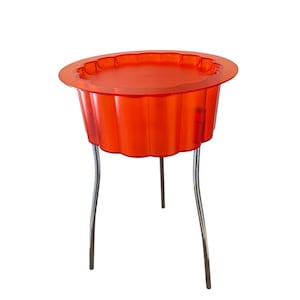 Peut inclure: Une table d'appoint dotée d'un plateau circulaire orange vif et translucide avec un bord festonné et cannelé. Le plateau est soutenu par trois pieds métalliques argentés et fins qui s'étendent vers le bas, assurant la stabilité.