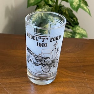 May include: A frosted glass with a black and white illustration of a Model T Ford from 1910. The glass has a white background with black lettering that reads "Model "T" Ford 1910".