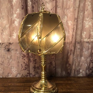 May include: A gold table lamp with a geometric patterned glass shade. The lamp has a round base and a single bulb.
