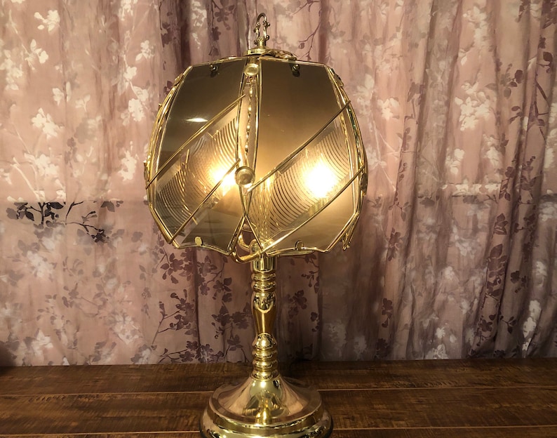 May include: A gold table lamp with a geometric patterned glass shade. The lamp has a round base and a single bulb.