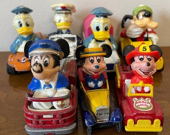 May include: A collection of vintage toy cars featuring Disney characters, including Mickey Mouse, Donald Duck, and Goofy. The cars are in various colors, including red, yellow, blue, and orange. Each car has a different design and features a unique character.