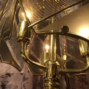 May include: A gold-toned table lamp with a geometric patterned glass shade. The lamp has a curved arm and a round base.