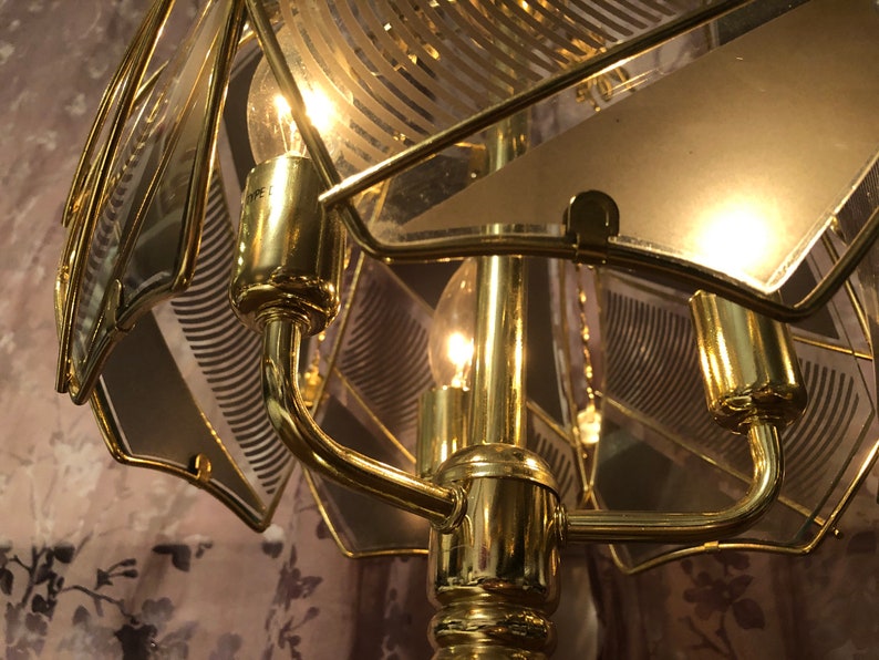 May include: A gold-toned table lamp with a geometric patterned glass shade. The lamp has a curved arm and a round base.